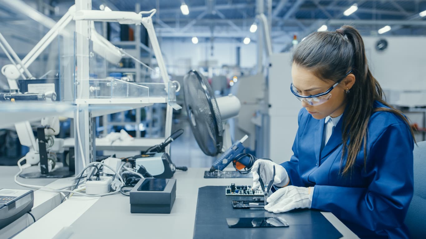 Young Female Blue and White Work Coat is Using Plier to Assemble Printed Circuit Board for Smartphone. Electronics Factory Workers in a High Tech Factory Facility