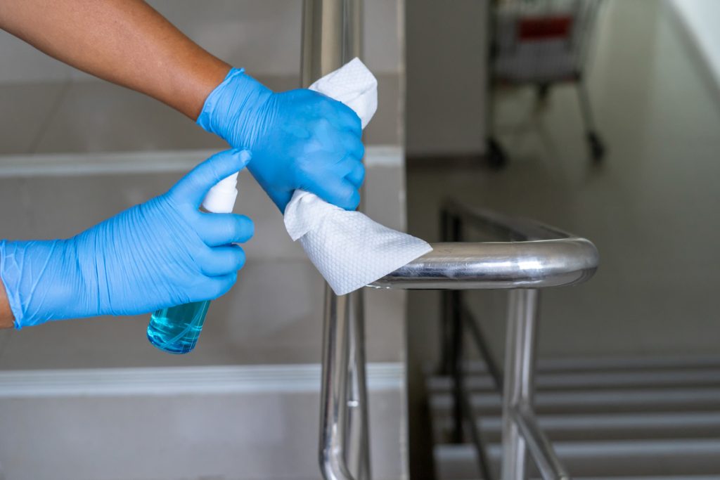 Close up of female hand using wet wipe and hand sanitizer spray to clean stainless steel staircase railing.Antiseptic,disinfection ,cleanliness and heathcare, anti virus concept.Anti bacterial and Corona virus (COVID-19).